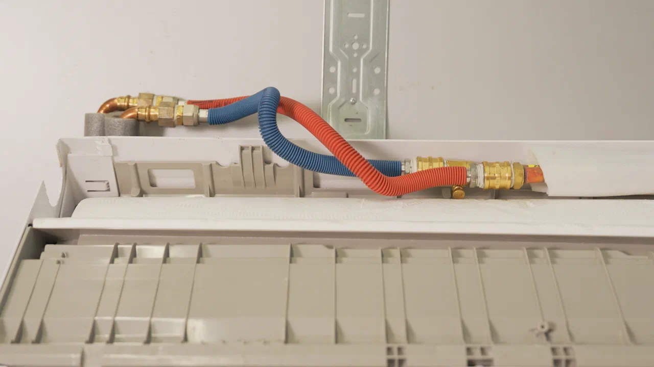 Red and blue pipes connected to a wall-mounted fan coil unit